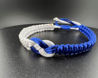 May include: A white and blue braided bracelet with a knot design. The bracelet is made of two strands of cord, one white and one blue, that are braided together.