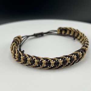 May include: A brown and tan braided bracelet with a woven pattern.