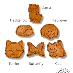 May include: A collection of brown, animal-shaped cookie cutters, including a llama, hedgehog, retriever, terrier, butterfly, and cat. Each cutter is labeled with its corresponding name. The image also includes a logo for Denton Creek Gardens.