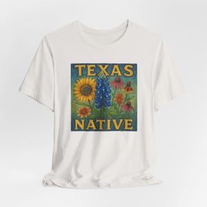 May include: White t-shirt featuring a colorful graphic of Texas wildflowers, including a sunflower and bluebonnets, with the words "TEXAS NATIVE" in gold lettering on a teal background. The shirt is made of a soft, comfortable material.
