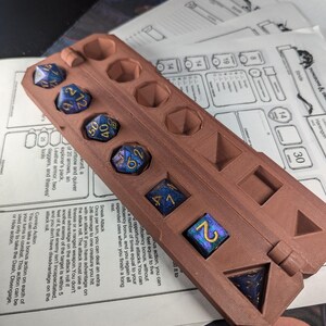 May include: A brown, 3D printed dice tray with a hinged lid. The tray has eight compartments for holding dice. The tray is open and several blue and gold dice are visible inside.
