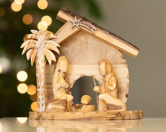 May include: A wooden nativity scene featuring a palm tree, Mary, Joseph, and the baby Jesus in a manger. The scene is set in a small wooden house with a star on top that reads "Bethlehem".