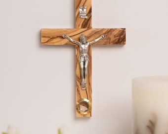 May include: A wooden crucifix with a silver figure of Jesus Christ. The cross is made of olive wood with a natural grain pattern. The figure is detailed, with arms outstretched. The top of the cross has a small metal plaque with the letters INRI.