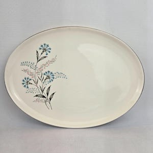 May include: A white oval serving platter with a silver rim and a floral design featuring blue and pink flowers.