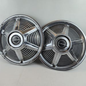 Puede incluir: Dos tapacubos Mustang vintage. Los tapacubos son plateados con un diseño de estrella y un centro negro con la palabra "MUSTANG" en blanco. Los tapacubos tienen un borde exterior acanalado.