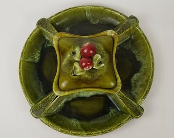 Puede incluir: Un plato de servir de cerámica verde con cuatro secciones y un compartimento central con tapa. El plato está decorado con un diseño en relieve de hojas verdes y bayas rojas.
