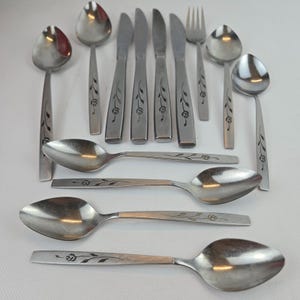May include: A set of stainless steel cutlery, comprising spoons, knives, and a fork. Each item has a floral pattern on the handle. The spoons have a rounded bowl, and the knives have a serrated edge.