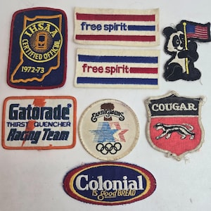 May include: A collection of vintage patches with various designs and text. Includes patches with the text "Free Spirit", "Gatorade Racing Team", "Colonial is good Bread", and a panda holding a flag. Other patches feature the text "IHSA Certified Official 1972-73" and "Cougar".