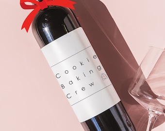 May include: A bottle of red wine with a white label that says "Cookie Baking Crew". The bottle is tied with a red ribbon bow.