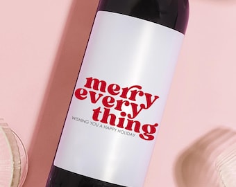 May include: A bottle of red wine with a white label that says "merry every thing" and "wishing you a happy holiday". The bottle is surrounded by four clear glass wine glasses on a pink background.