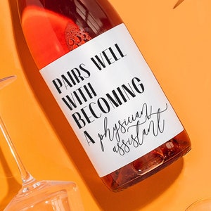 May include: A bottle of rose wine with a white label that says "Pairs well with becoming a physician assistant". The bottle is surrounded by four clear wine glasses on a bright orange background.