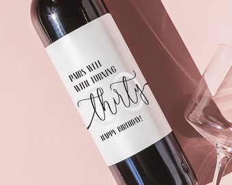 May include: A white wine bottle label with black text that reads "Pals with turning thirty. Happy birthday!" The bottle is on a pink background with two wine glasses.