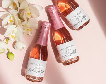 May include: Three mini bottles of pink champagne with white labels that say "Ain't no party like a bridal party!" The bottles are on a pink background with white orchids.