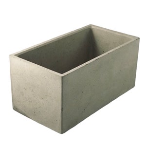 May include: A rectangular concrete planter with a rough, textured surface. The planter is empty and ready for planting.