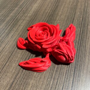 May include: A 3D printed red rose sculpture with intricate details. The rose is curled into a spiral shape and has a textured surface.