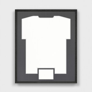 Op de afbeelding: Een zwart frame met een witte passe-partout en een uitsparing in de vorm van een T-shirt. De passe-partout is ontworpen om een T-shirt te houden voor weergave.