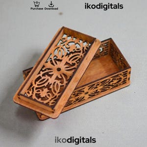 Peut inclure: Petite boîte en bois ouverte avec un couvercle à charnière. Le couvercle et les côtés présentent des motifs floraux complexes découpés au laser. La boîte est en bois brun clair et est partiellement ouverte. Le texte "ikodigitals" est visible.