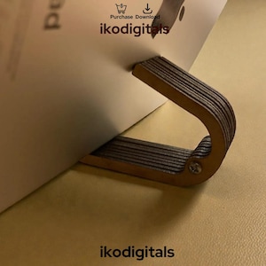 Puede incluir: Un atril de madera con un asa curvada, sosteniendo una página blanca. El soporte está hecho de madera en capas y está asegurado con un tornillo. El texto "ikodigitals" es visible en la parte inferior.