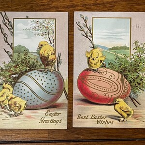 Op de afbeelding: Twee vintage paaspostkaarten. Eén toont een geel kuiken op een blauw en wit ei, met de tekst "Easter Greetings". De andere toont een kuiken op een rood ei, met de tekst "Best Easter Wishes".