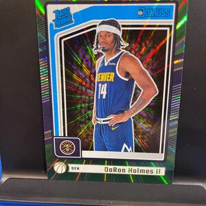 May include: A basketball trading card featuring DaRon Holmes II in a Denver Nuggets uniform. The card has a green and blue border with the words "Rated Rookie" and "Donruss". The player is wearing a white headband and the number 14.