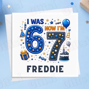 May include: A square birthday greeting card featuring the text I WAS 67 NOW I'M 67 and the name FREDDIE. The design includes a large blue number 6, a large dark blue number 7, birthday balloons, a gift box, a cake with a candle, and stars.