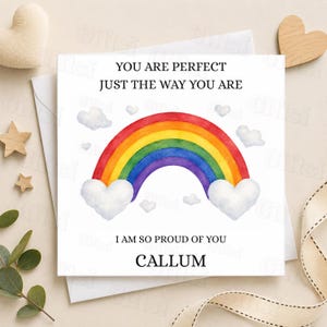 May include: A white greeting card featuring a rainbow design and the text "YOU ARE PERFECT JUST THE WAY YOU ARE" and "I AM SO PROUD OF YOU CALLUM". The rainbow is in vibrant colours.