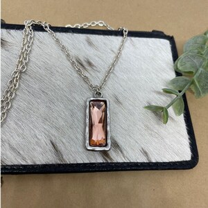 May include: A silver chain necklace with a rectangular pendant featuring a large, faceted, peach-colored gemstone.