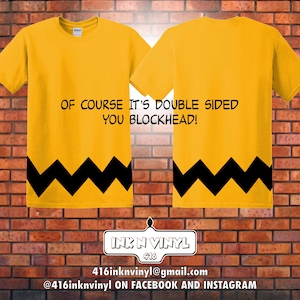 May include: Mustard yellow t-shirt featuring a black zig-zag design at the hem and the text "OF COURSE IT'S DOUBLE SIDED YOU BLOCKHEAD!". The image shows the front and back of the shirt. A logo with contact details is at the bottom.