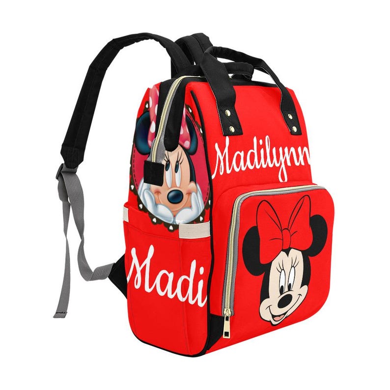 May include: Red backpack featuring Minnie Mouse graphics and the names "Madi" and "Madilynn" in white script. The bag has black straps and a zipper closure. A large Minnie Mouse face is on the front pocket.