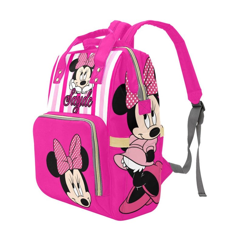 May include: Pink backpack featuring Minnie Mouse illustrations. The bag has a front pocket with a Minnie Mouse graphic, a striped section, and the name "Sayde". Adjustable shoulder straps and a top handle are included.