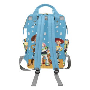 May include: A light blue backpack featuring characters from the Toy Story movie. The backpack has a light blue background with white clouds. The backpack has two side pockets and adjustable shoulder straps.