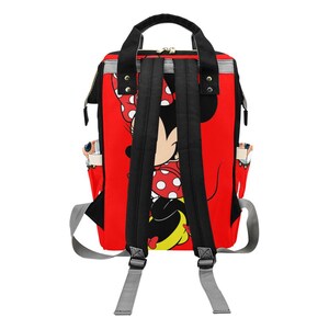 May include: Red backpack featuring a Minnie Mouse design. The backpack has black straps, a black handle, and gray shoulder straps. The Minnie Mouse graphic includes a red bow with white polka dots. The backpack has side pockets.
