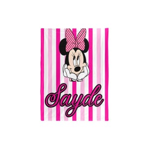 May include: A pink and white striped blanket featuring Minnie Mouse with a pink polka dot bow. The blanket has the name "Sayde" in a cursive font. The blanket is a vibrant and colorful item.