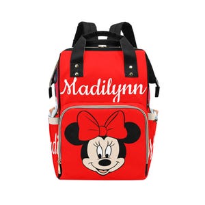 May include: Red backpack featuring a Minnie Mouse graphic with a large bow. The backpack has black straps and handles, side pockets, and the name "Madilynn" in white script across the top. A stylish and functional bag.