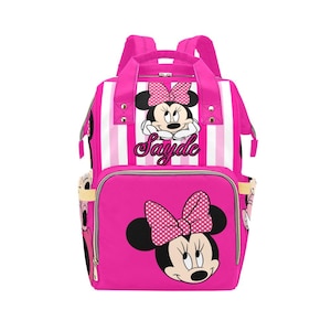 May include: Pink backpack featuring Minnie Mouse. The backpack has a large front pocket with a Minnie Mouse graphic and a polka dot bow. The top section has white and pink stripes and the text "Sayde".