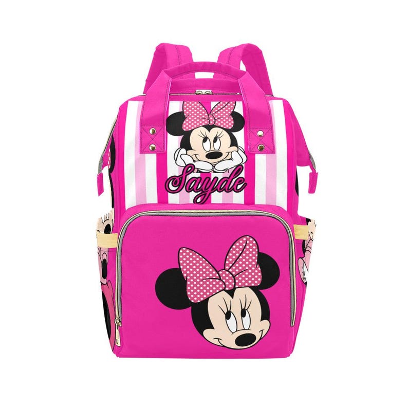 May include: Pink backpack featuring Minnie Mouse. The backpack has a large front pocket with a Minnie Mouse graphic and a polka dot bow. The top section has white and pink stripes and the text "Sayde".