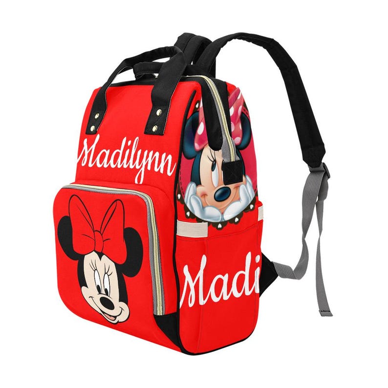 May include: Red backpack featuring Minnie Mouse graphics and the name "Madilynn" in white script. The bag has black straps, a front pocket with a Minnie Mouse bow, and a side pocket. The backpack is designed for carrying baby essentials.