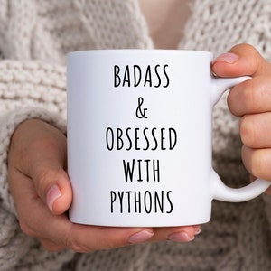 May include: White ceramic mug with black text that reads "Badass & Obsessed with Pythons".
