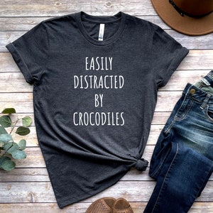 May include: A dark gray t-shirt with the text "Easily Distracted By Crocodiles" printed in white.