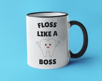 May include: White ceramic mug with a black rim and handle. The mug features a cartoon tooth with floss and the text "Floss Like A Boss" printed on it.