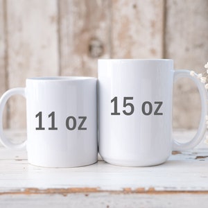 May include: Two white ceramic mugs with black text. The mug on the left says "11 oz" and the mug on the right says "15 oz".