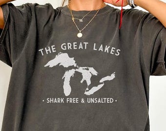 Op de afbeelding: Donkergrijs T-shirt met de tekst "THE GREAT LAKES" en een witte afbeelding van de Grote Meren. Daaronder staat "SHARK FREE & UNSALTED". Het T-shirt heeft een relaxte pasvorm.