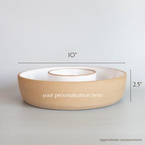 May include: A round ceramic serving dish with a tan exterior and white interior, featuring a central circular compartment. The text 'your personalisation here' is printed on the side. Dimensions are 25.4 cm in diameter and 6.35 cm in height.