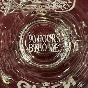 May include: Clear glass with the text "90 HOURS BTHO ME!" etched on the bottom. The glass has a wide, rounded shape and a textured surface. The top rim of the glass has a decorative design.