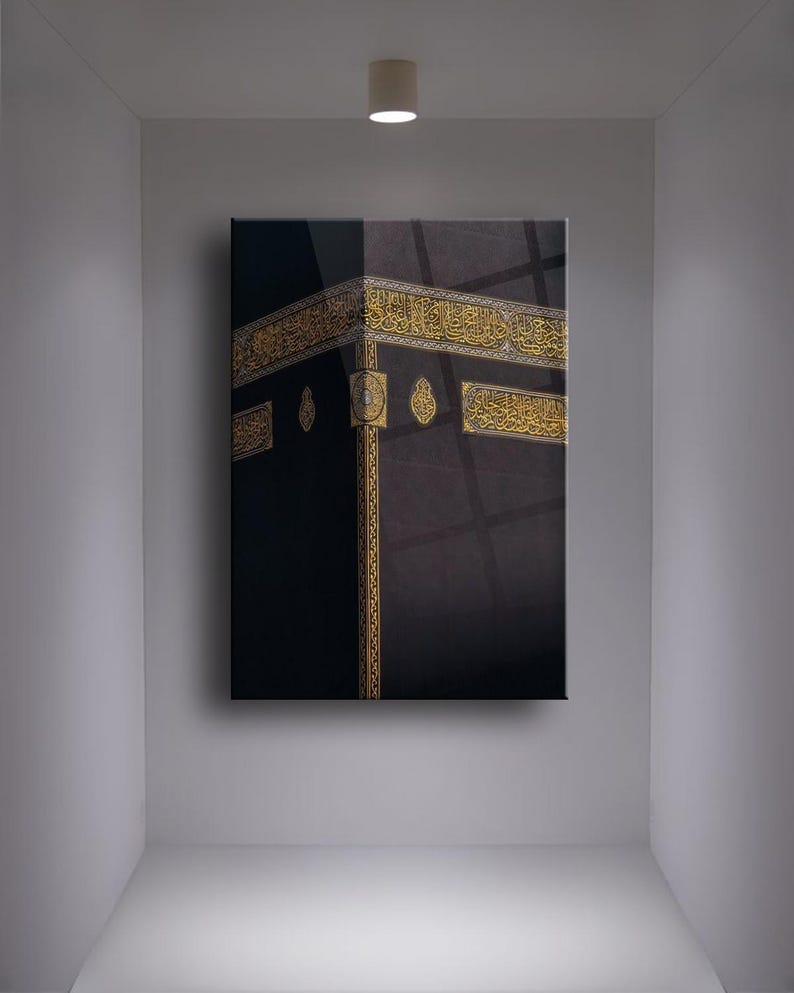 May include: A black and gold framed canvas print of the Kaaba, a cube-shaped building in Mecca, Saudi Arabia, that is Islam's holiest place. The Kaaba is covered in black cloth and has gold trim. The print is framed in a black frame.