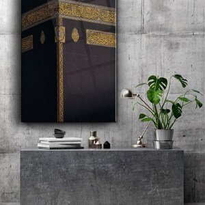 May include: A black and gold framed print of the Kaaba, a cube-shaped building in Mecca, Saudi Arabia. The Kaaba is considered the holiest site in Islam and is a destination for Muslim pilgrims.