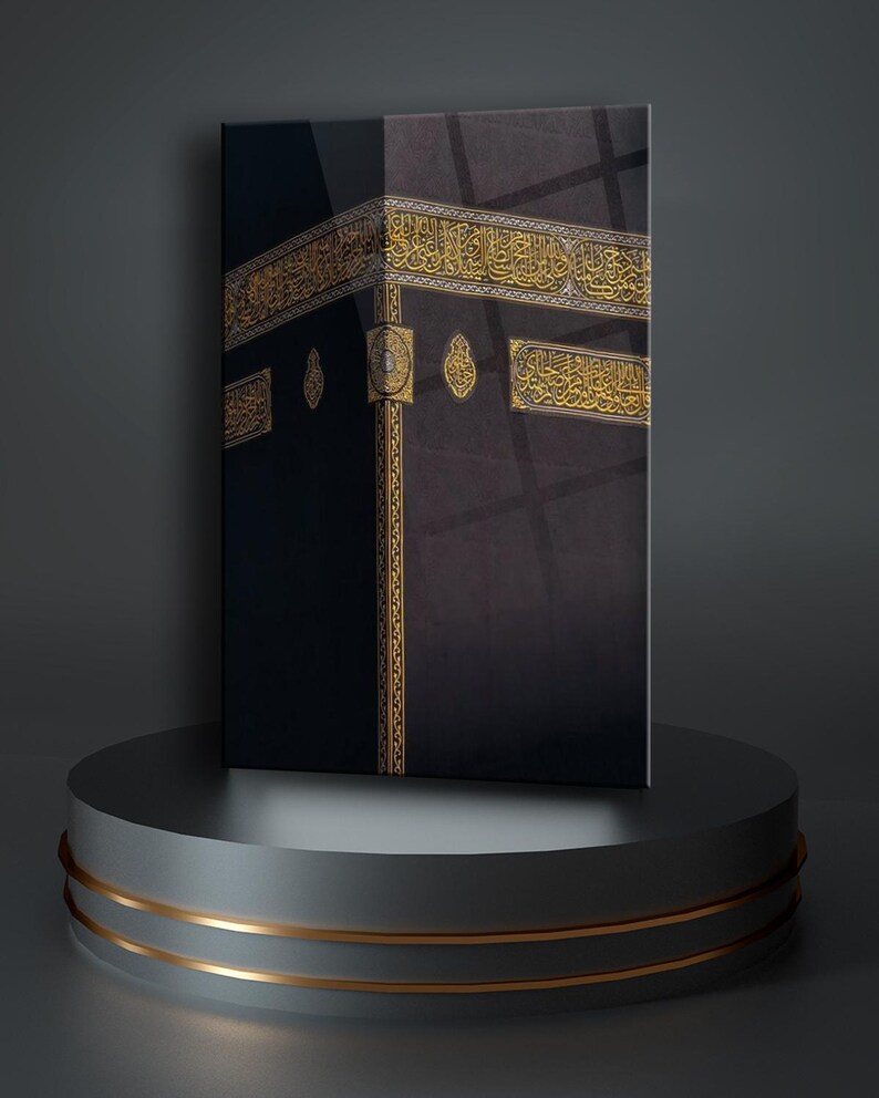 May include: A black and gold framed canvas print of the Kaaba, a cube-shaped building in Mecca, Saudi Arabia. The Kaaba is covered in black cloth and decorated with gold inscriptions in Arabic.