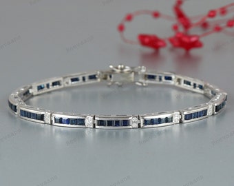 May include: A silver bracelet featuring rectangular, dark blue gemstones and small, round, clear gemstones. The bracelet is secured with a clasp. The bracelet is displayed on a light grey surface.