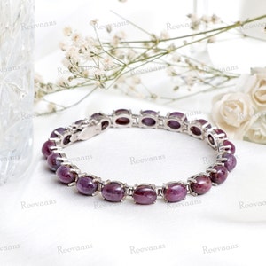 May include: A silver bracelet featuring a row of oval-shaped purple gemstones. The bracelet has a clasp fastening.
