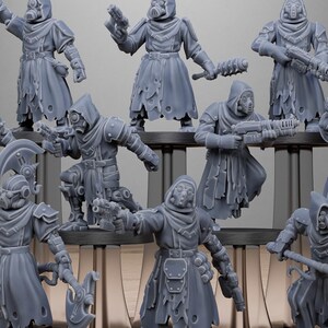 May include: A collection of gray miniature figurines of hooded figures, some with gas masks, holding weapons. The figures are on a black base, with the word "STATIONFORGE" and a skull logo in the background.
